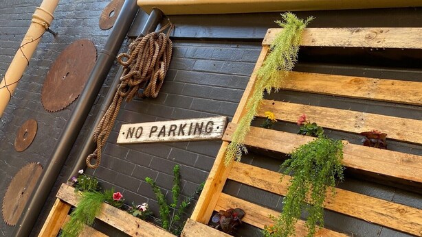 A wooden bench with a 'NO PARKING' sign, a rope, and a small potted plant. - Royal Hotel (Horsham)
