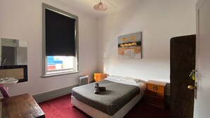 A bedroom with a bed, a dresser, a mirror, a window with a view, and a painting on the wall. - Royal Hotel (Horsham)