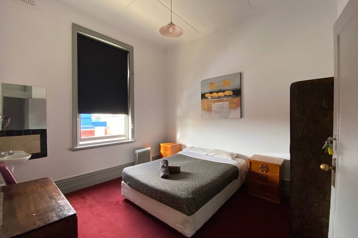 Un dormitorio con cama, cómoda, espejo, ventana con vista y un cuadro en la pared.