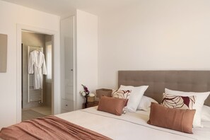 A hotel room with a bed, pillows, a nightstand, a vase with flowers, and a robe hanging on a rack. - Villa TourterelleLuxurious villa with breathtaking sea views! (Roquebrune-sur-Argens)