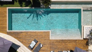 En vy från ovan av en rektangulär swimmingpool med klart vatten, omgiven av ett trädäck.