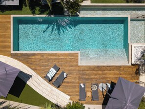 Eine Vogelperspektive auf einen rechteckigen Swimmingpool mit klarem Wasser, umgeben von einer Holzterrasse.
