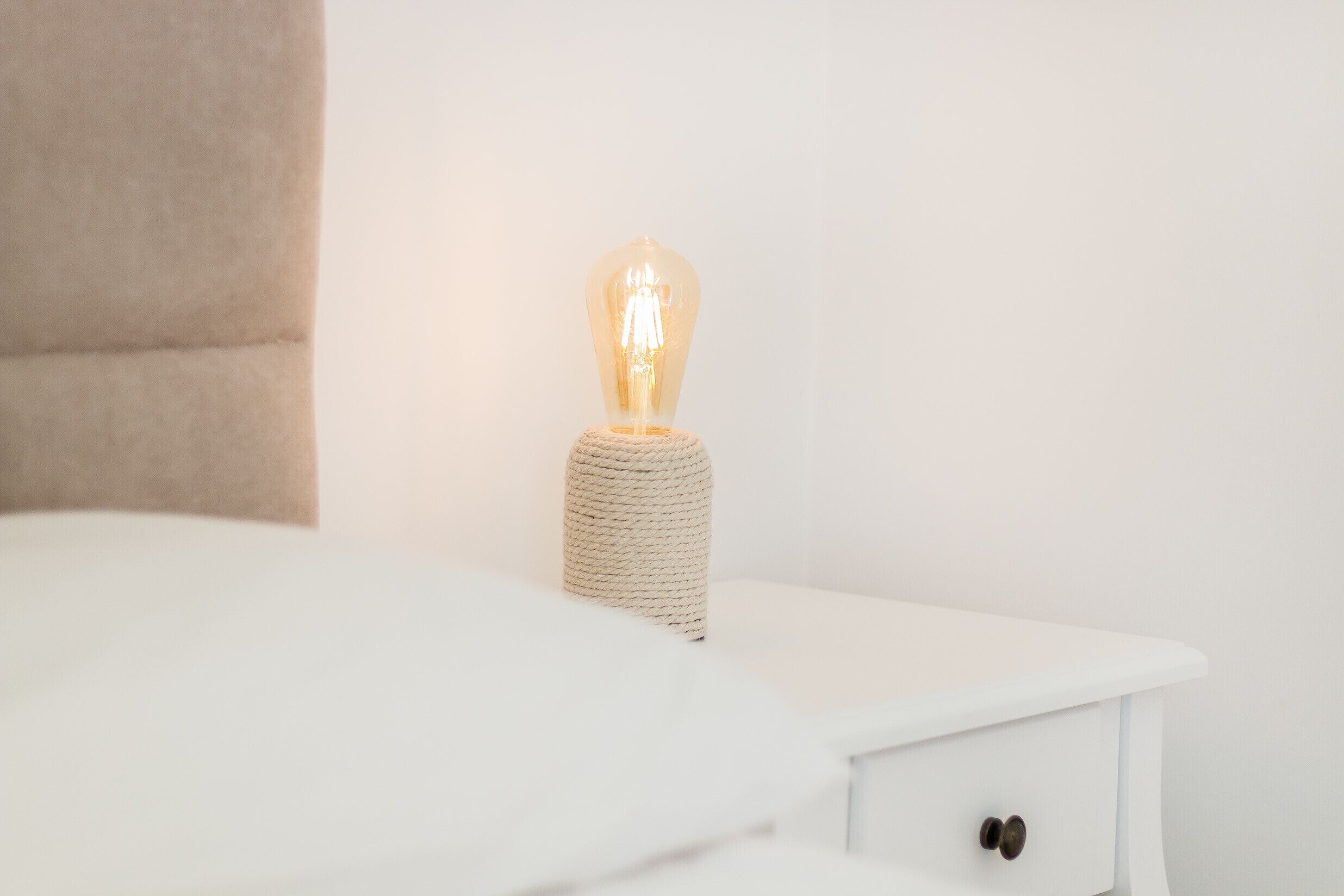 Ein weißer Nachttisch mit einer einzelnen Glühbirnenlampe darauf.