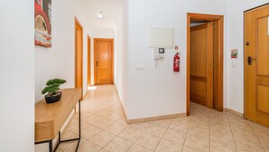 A hallway with a wooden bench, a potted plant, a fire extinguisher, and a fire alarm.