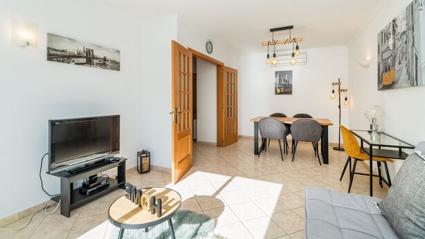 A modern living room with a flat-screen TV, a dining area with a table and chairs, and a sofa.