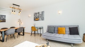 A modern living room with a sofa, dining table, chairs, and a hanging light fixture.