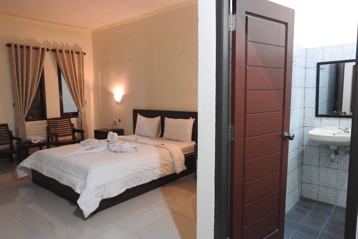 Hotelkamer met een bed, nachtkastje, stoel, bureau en een badkamer met wastafel en spiegel.