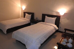 A hotel room with two single beds, each with white bedding and headboards. There is a nightstand with a lamp and a tray with tea cups and a teapot. - D'Batur Hotel Lombok (Senggigi)