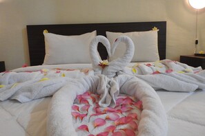A neatly made bed with a heart-shaped towel arrangement and rose petals. - D'Batur Hotel Lombok (Senggigi)