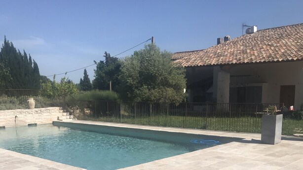 A swimming pool with tiled flooring, a table, and a chair. - Bastide Campagne Canal (Cucuron)