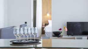 Un área de comedor con una bandeja de copas de vino vacías sobre una mesa de vidrio, un sofá, un televisor y una puerta de madera al fondo.