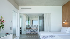 Habitación de hotel moderna con escritorio de vidrio, dos camas, zona de ducha y vistas a la ciudad.