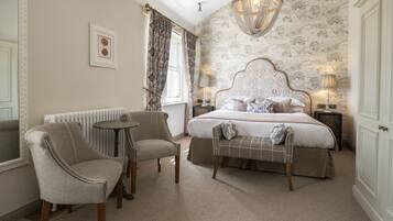 A bedroom with a large bed, two armchairs, a small table, and a chandelier.