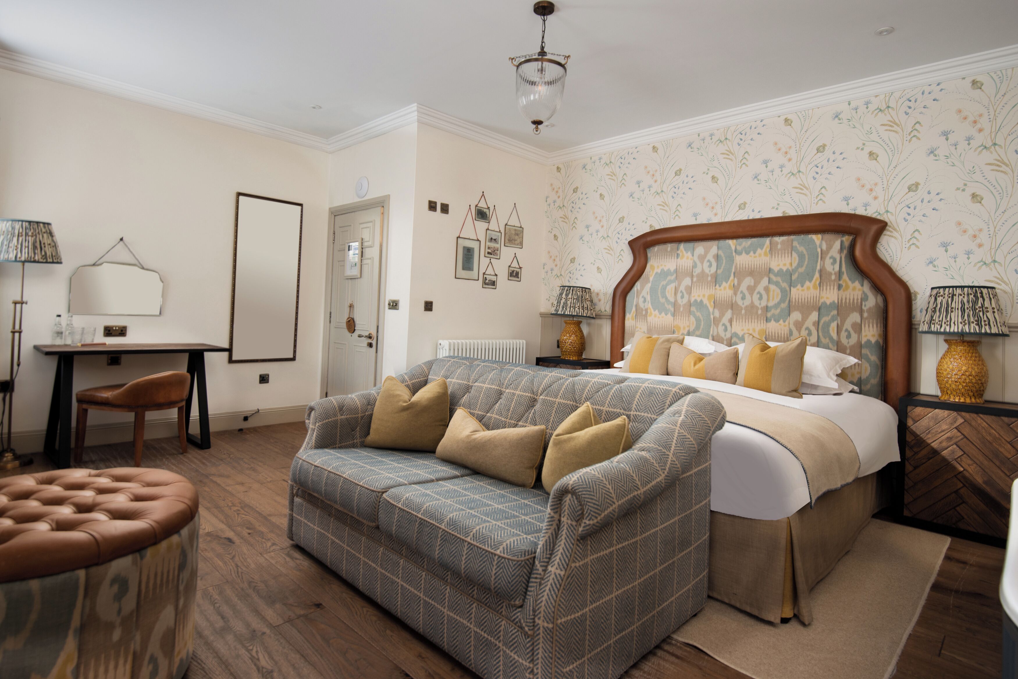 A bedroom with a bed, a sofa, a chair, a table, and a lamp.