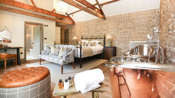 A spacious bedroom with a large bed, a wooden ceiling, a bathtub, and a seating area with a table and ottoman. - Beadnell Towers Hotel (Chathill)