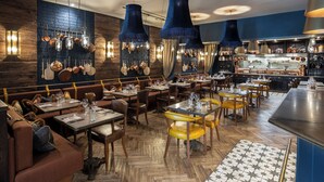 A restaurant with wooden walls, hanging pots, and blue pendant lights. Tables are set with yellow chairs and wooden floors. - Beadnell Towers Hotel (Chathill)