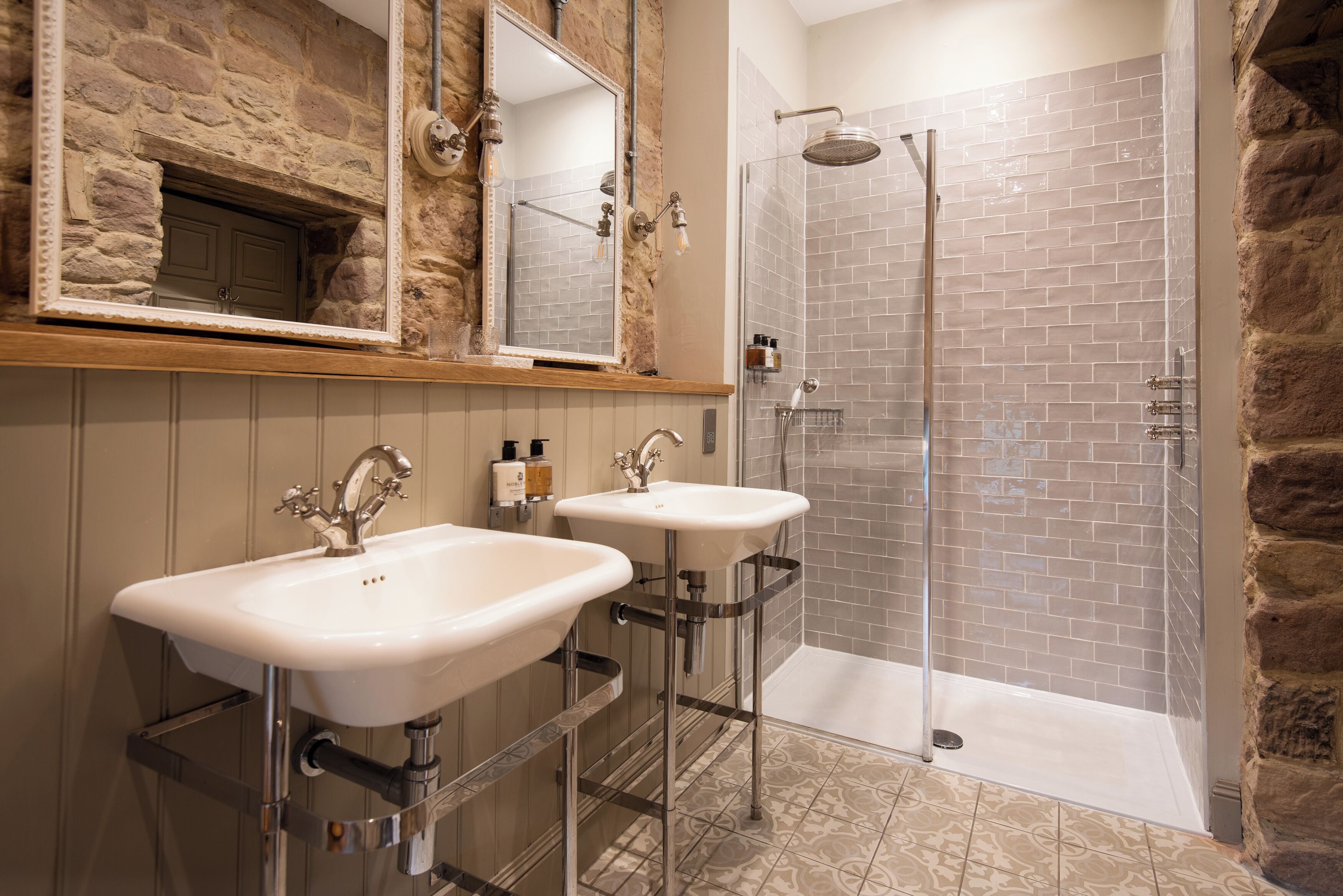 A bathroom with two sinks, a shower, and a mirror.