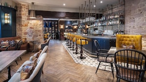 A bar area with a long counter, multiple stools, and a variety of bottles on shelves. - Beadnell Towers Hotel (Chathill)