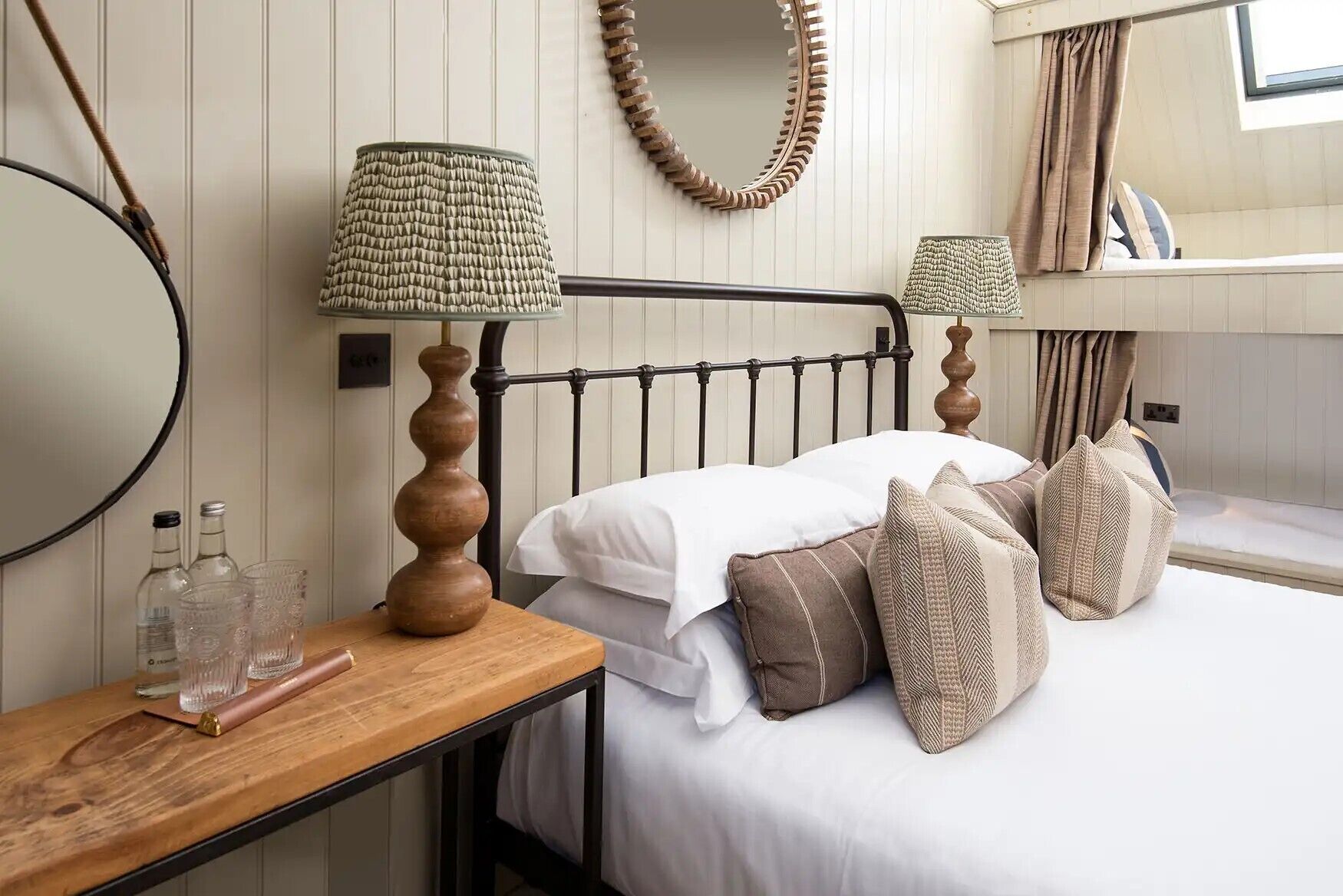 A neatly arranged bedroom with a bed, bedside lamps, a wooden nightstand, and a mirror.