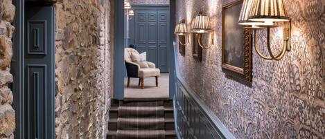A hallway with stone walls, a blue door, and a chair. There are steps leading to a door with a blue frame.