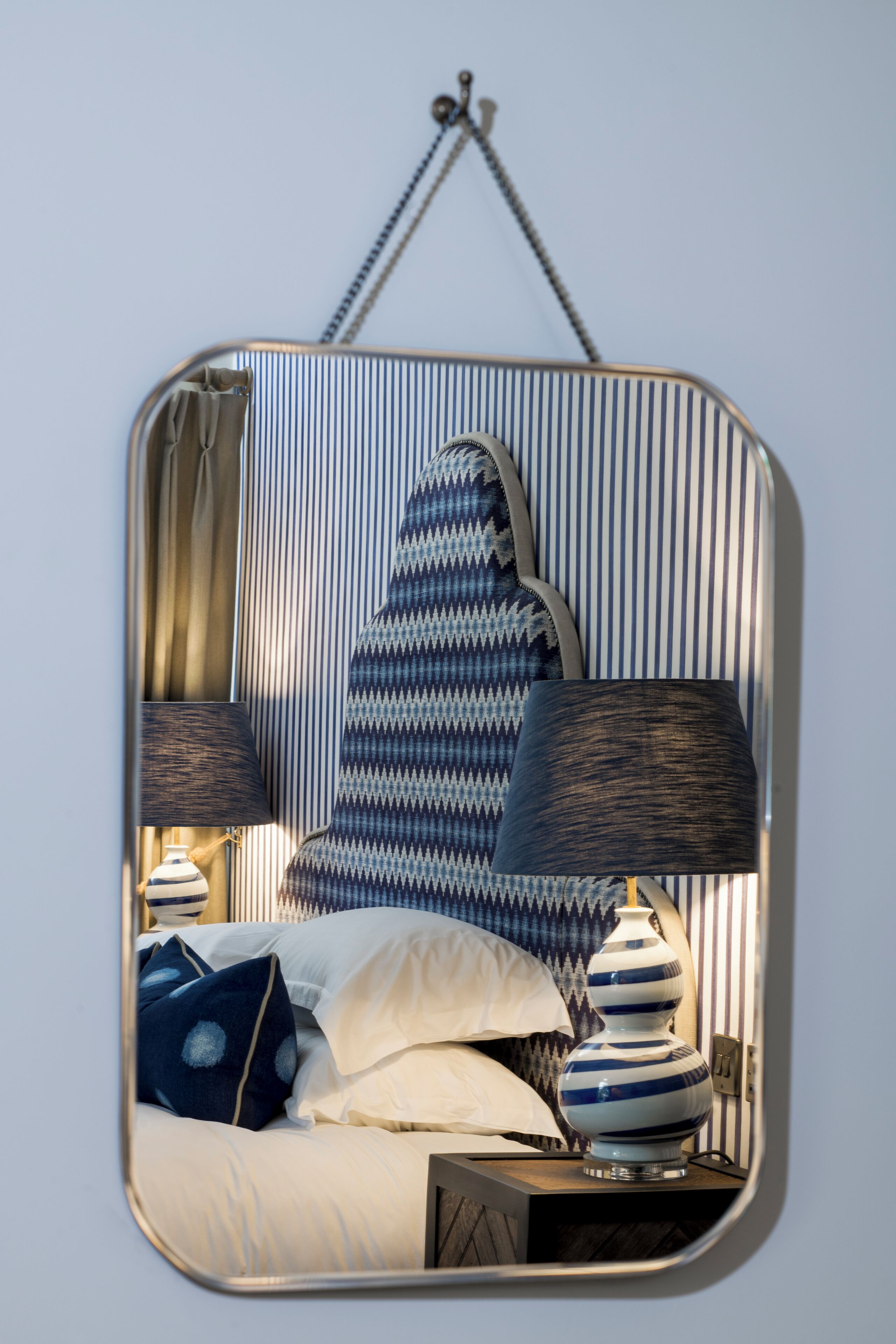 A mirror with a reflection of a bed, pillows, and a lamp.