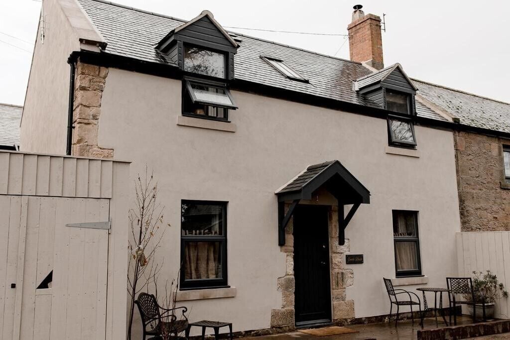 A two-story building with a white facade, a black door, and a small porch area with a table and chairs.