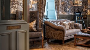 A traditional room with a patterned wallpaper, a classic armchair, a sofa, and a wooden floor. - Beadnell Towers Hotel (Chathill)
