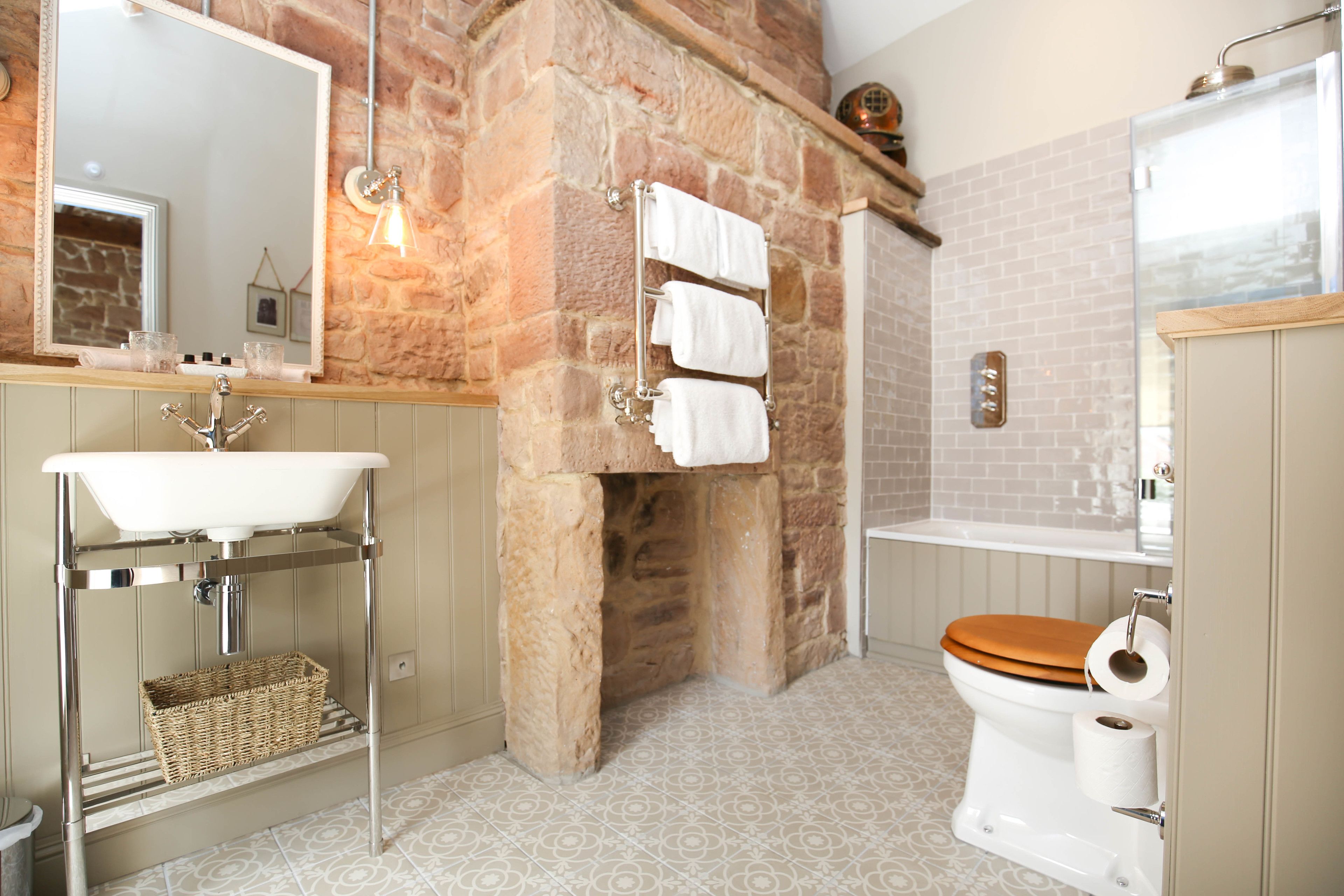 Ein Badezimmer mit Steinwand, einem Waschbecken mit Chromfuß, einer Holzwc und einem Spiegel über dem Waschbecken.