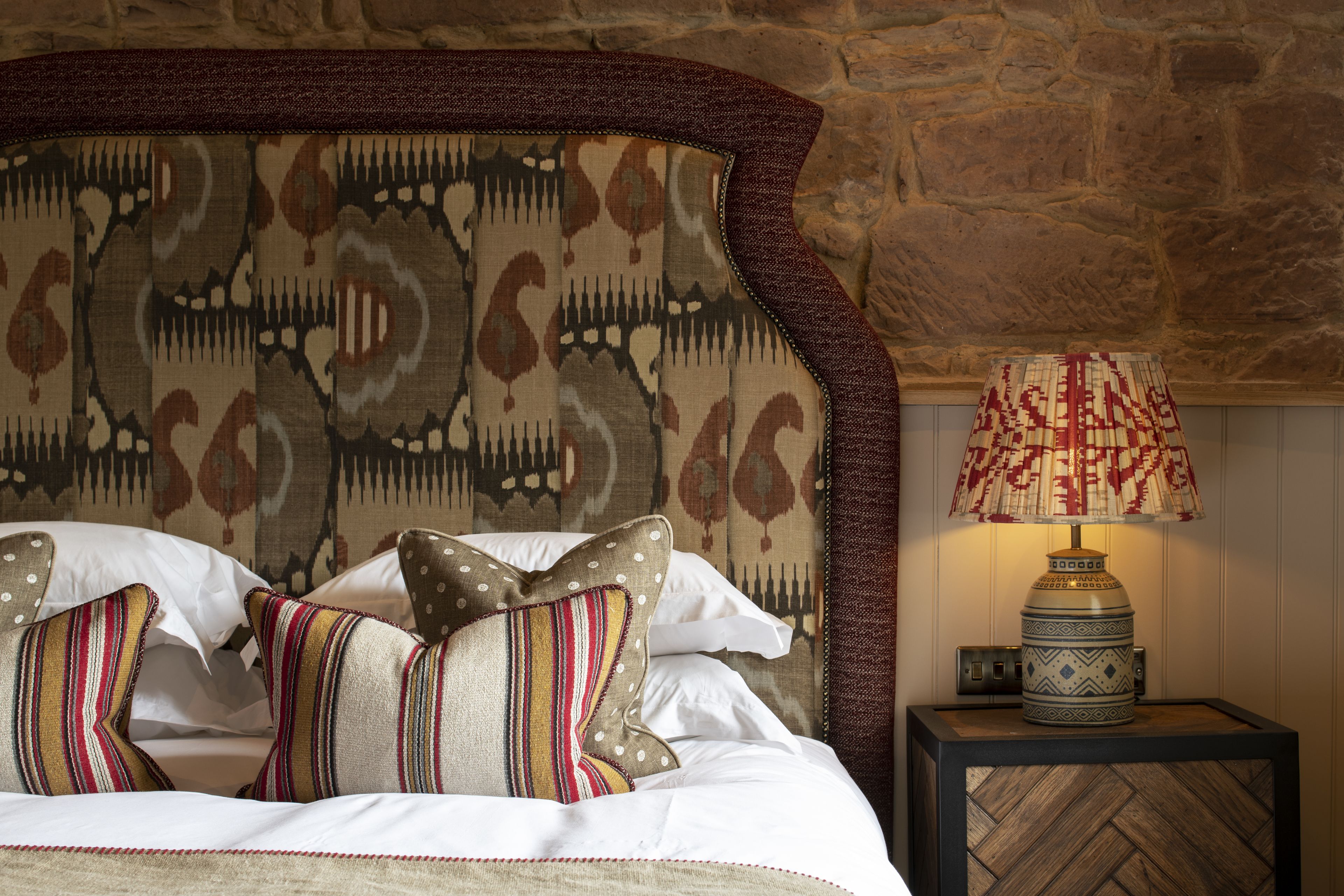 Un lit avec des coussins à motifs, une tête de lit décorative et une table de chevet avec une lampe.