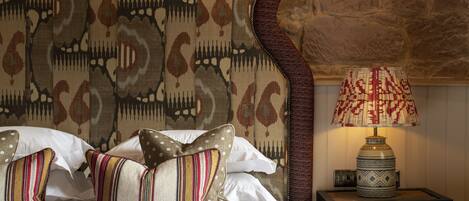 Un lit avec des coussins à motifs, une tête de lit décorative et une table de chevet avec une lampe.