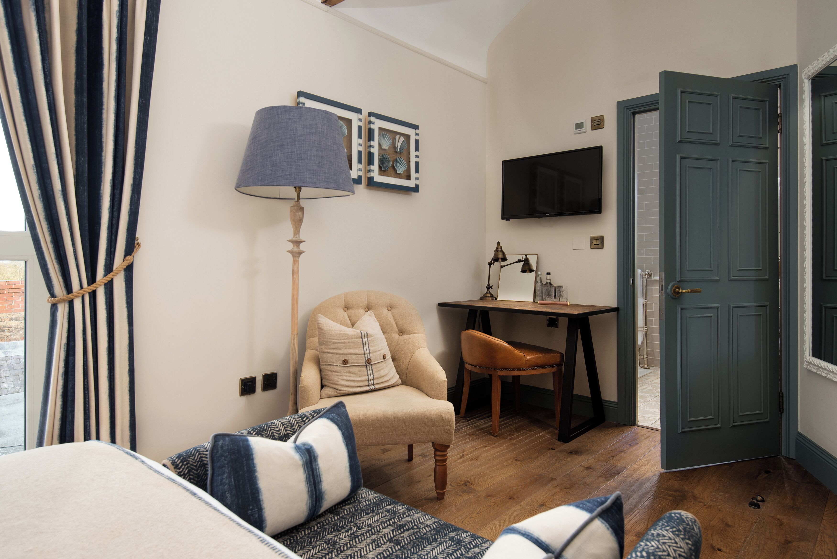A room with a bed, a chair, a desk, a lamp, a TV, and a door.