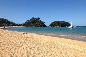 Una playa arenosa con agua azul cristalina, barcos y un faro a lo lejos.
