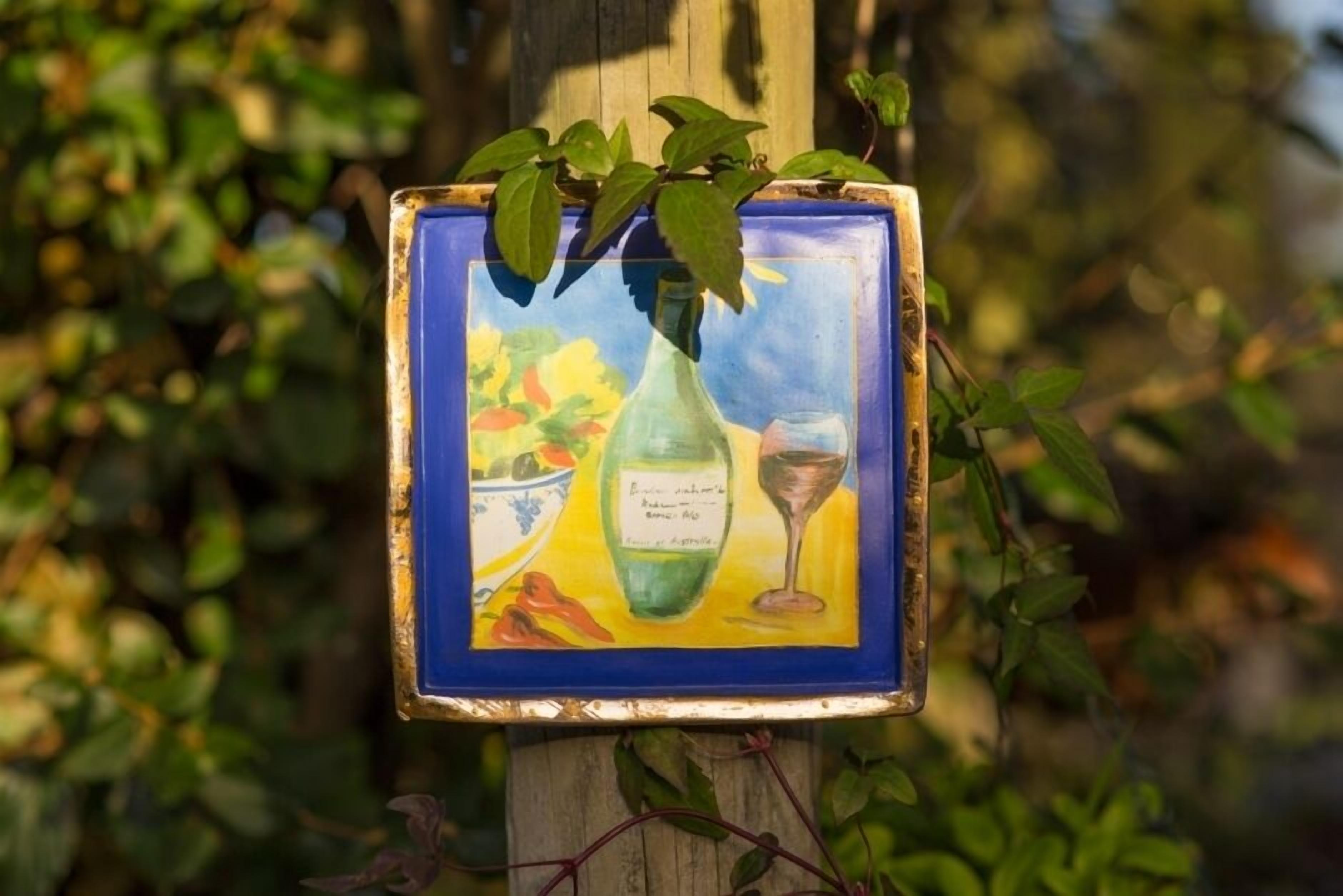 A framed artwork with a bottle and glass, surrounded by greenery.