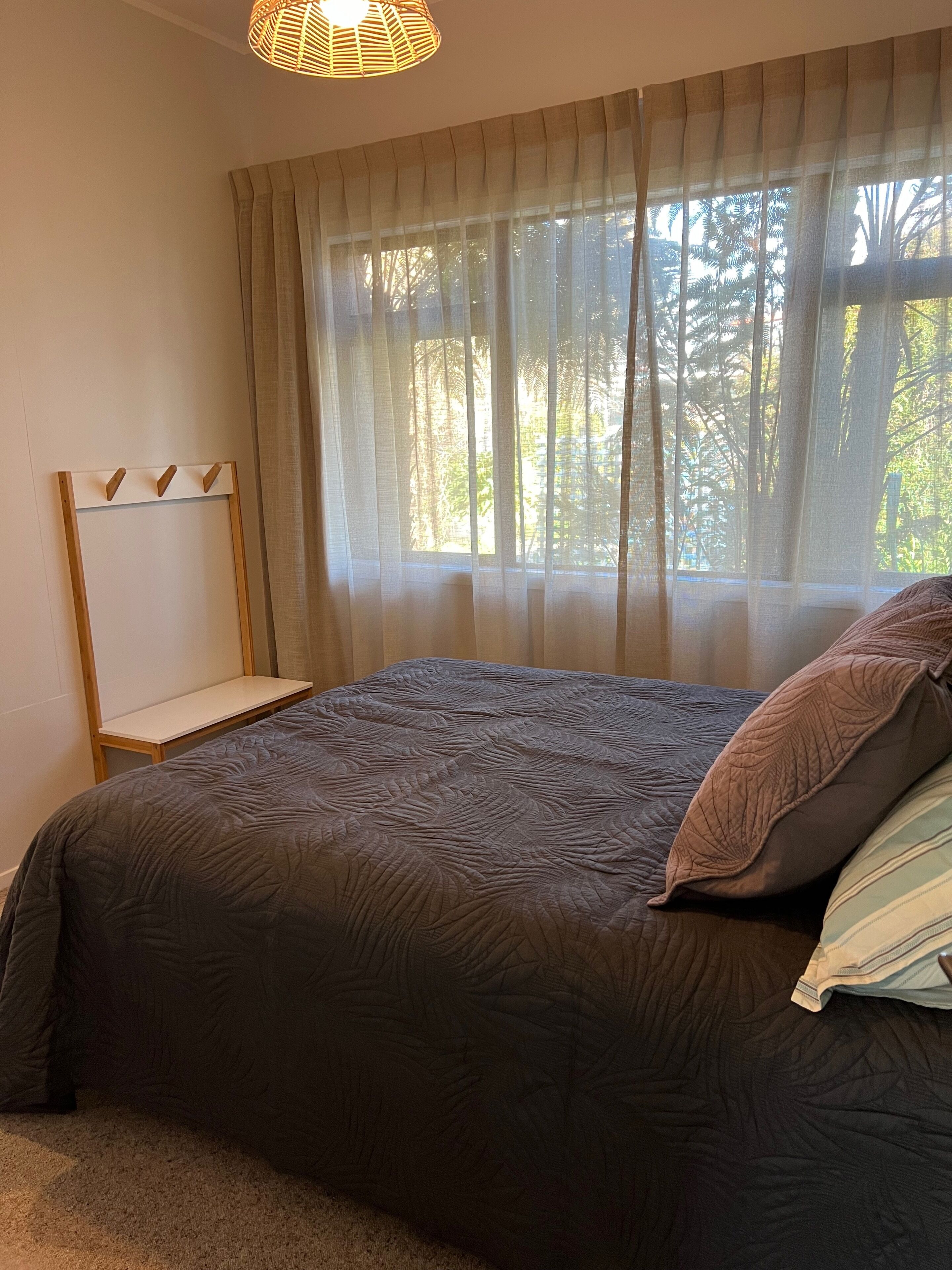 Une chambre à coucher avec un lit, une table de chevet et une fenêtre ornée de rideaux légers.