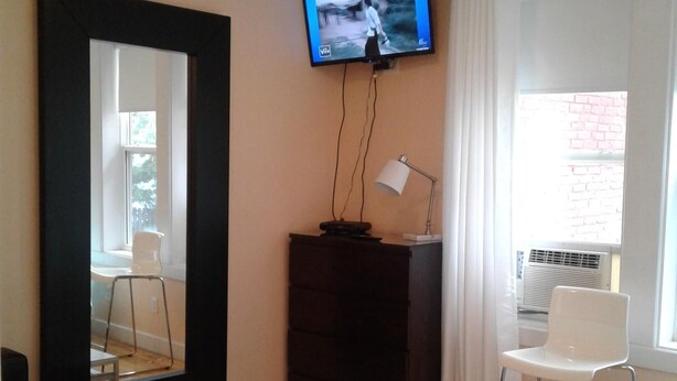 Hotelkamer met een aan de muur bevestigde televisie, een grote spiegel, een klein tafeltje, een stoel en een raam met gordijnen.