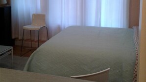 Een hotelkamer met een bed, een stoel, een bureau en een raam met gordijnen.