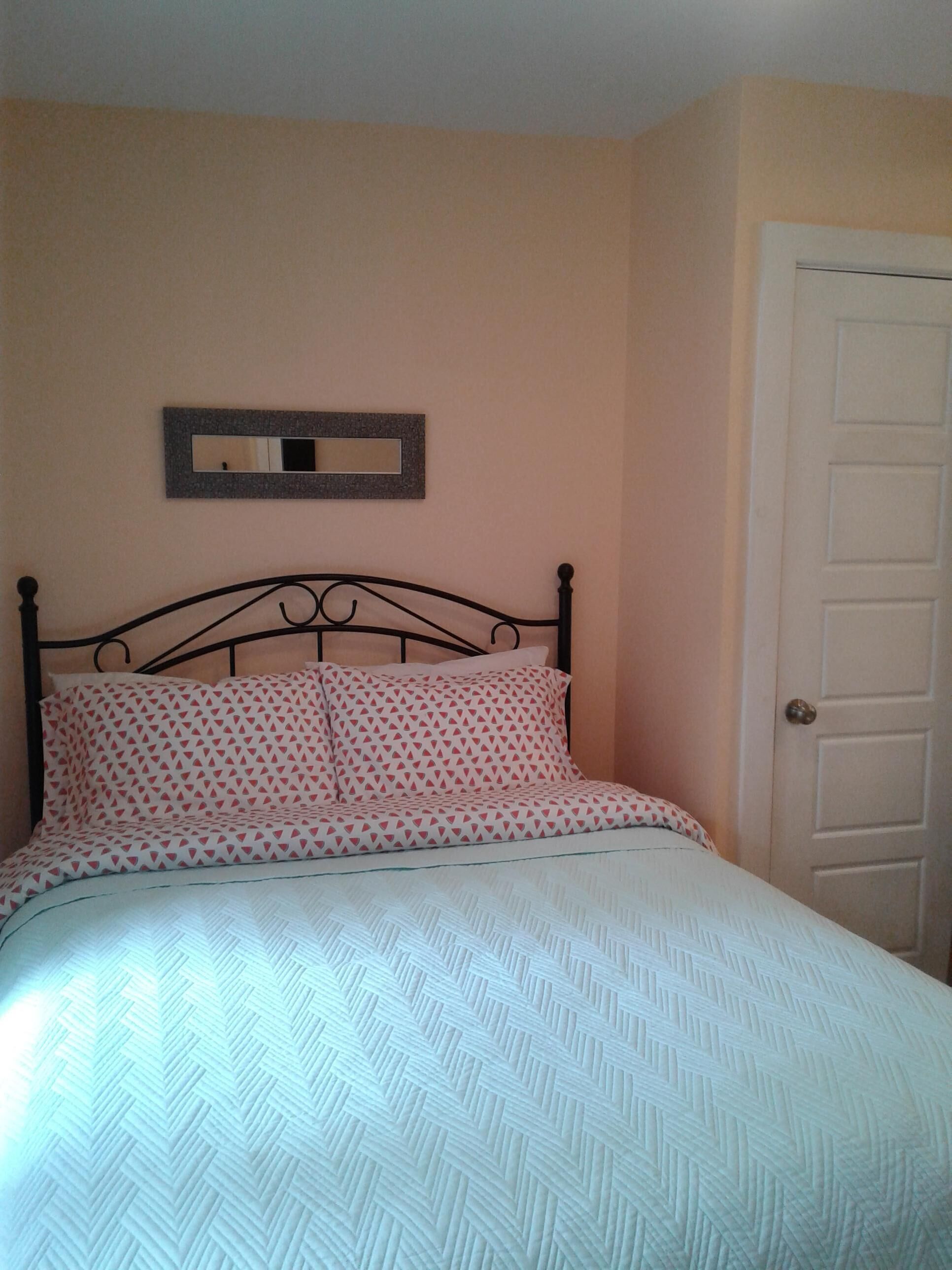 A bedroom with a bed, a door, and a wall-mounted mirror.