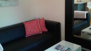 Een moderne woonkamer met een zwarte bank, een glazen salontafel en een schilderij aan de muur.