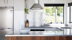Een moderne keuken met een groot eiland, witte kasten, een roestvrijstalen afzuigkap en uitzicht op het omliggende landschap door een raam.