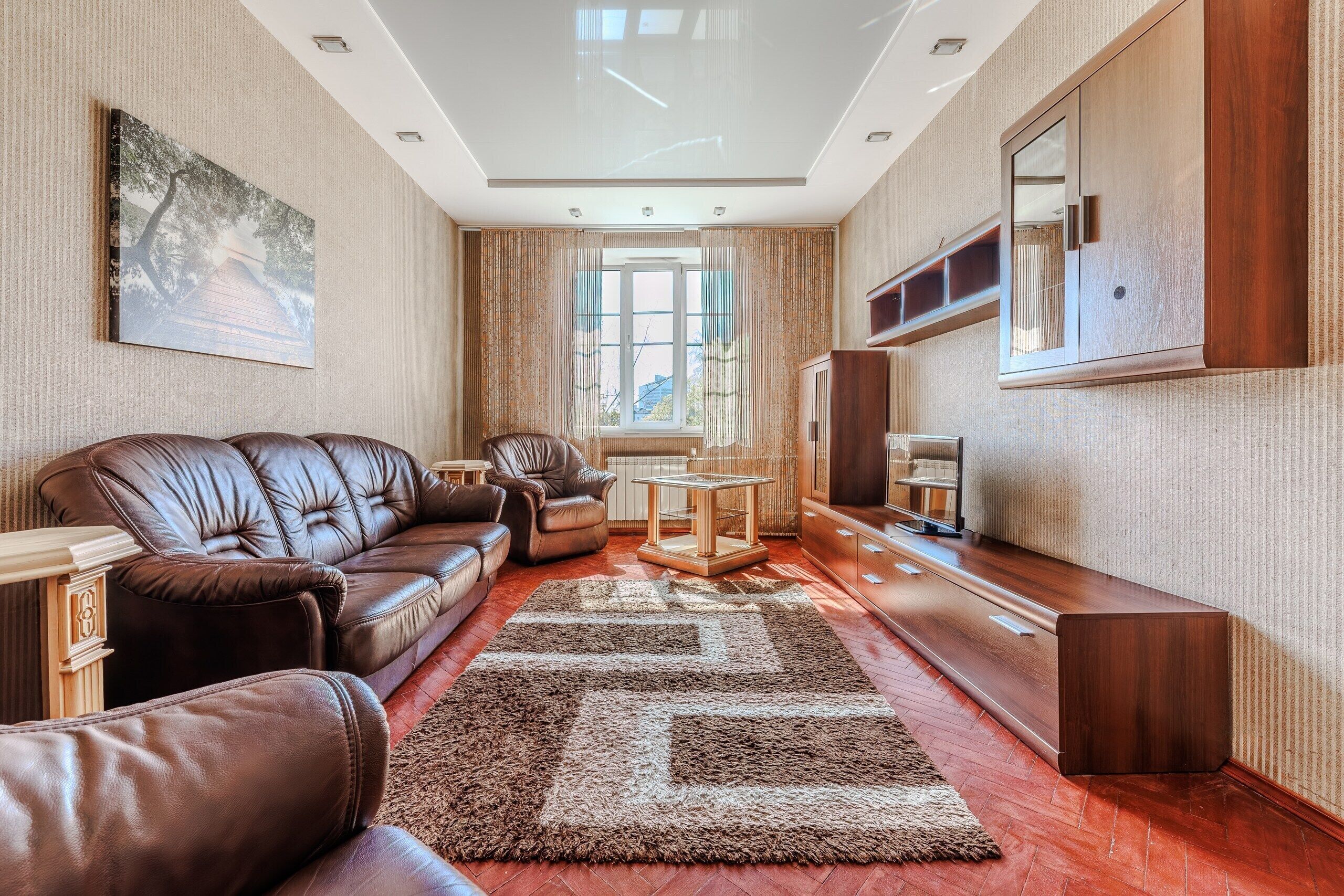 A living room with a brown leather sofa, a glass coffee table, and a large window with curtains.