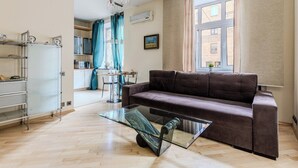Un salon moderne avec un canapé marron, une table basse en verre et un coin cuisine à l’arrière-plan.