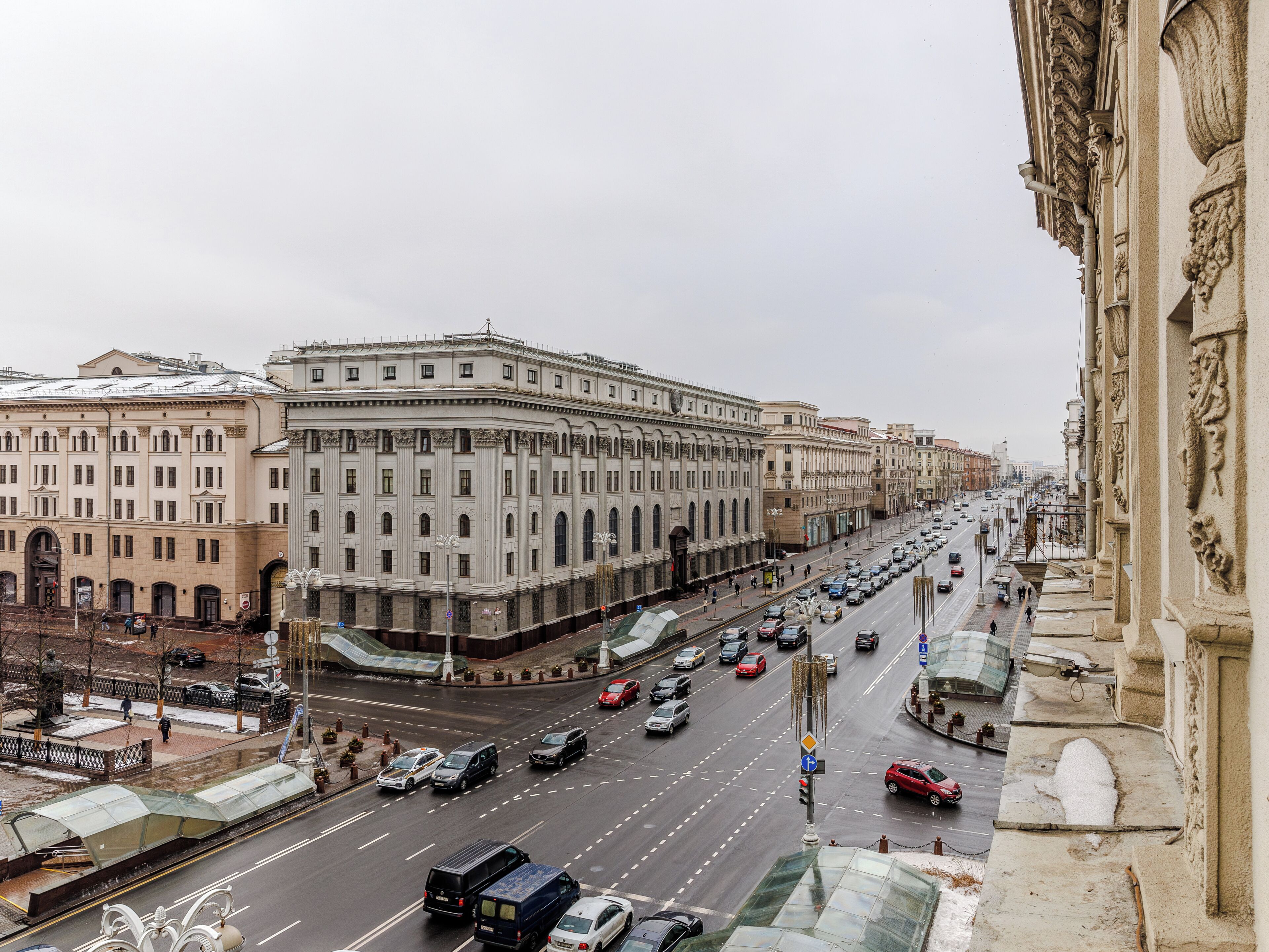 A busy urban street with classical architecture, a tram line, and a pedestrian walkway.