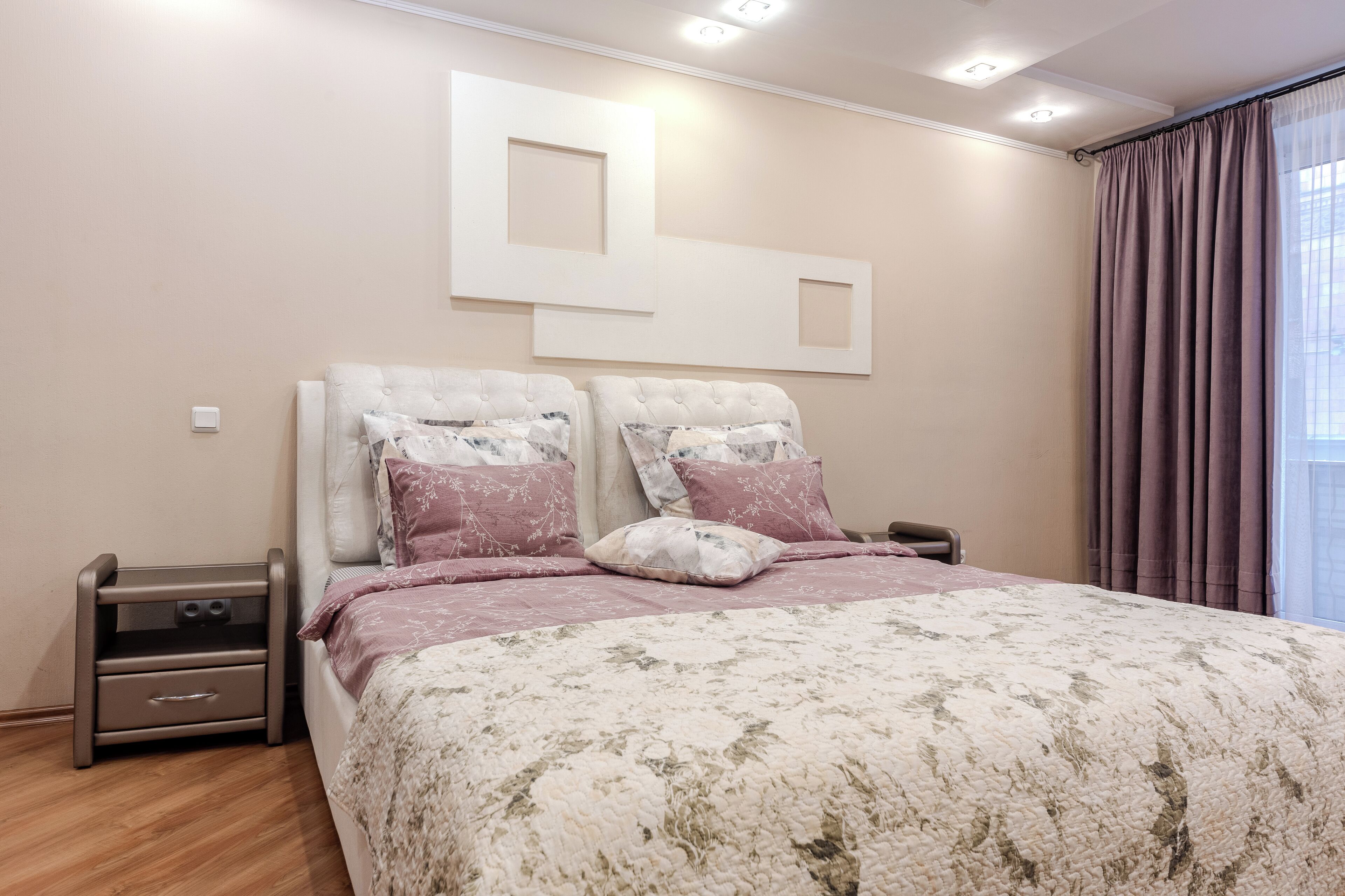 Une chambre avec un grand lit, deux tables de chevet, une œuvre d’art moderne accrochée au mur et une fenêtre avec des rideaux.