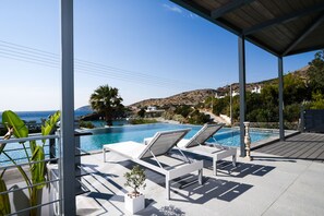 A poolside area with lounge chairs and a view of the sea. - Villa Selenia Platinum (Saronikos)