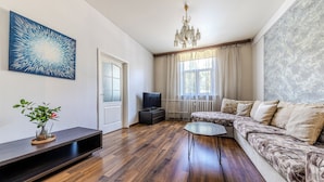 A modern living room with a wooden floor, a sectional sofa, a flat-screen TV, a decorative plant, and a large abstract painting. - StudioMinsk Apartments in Centre (Minsk)