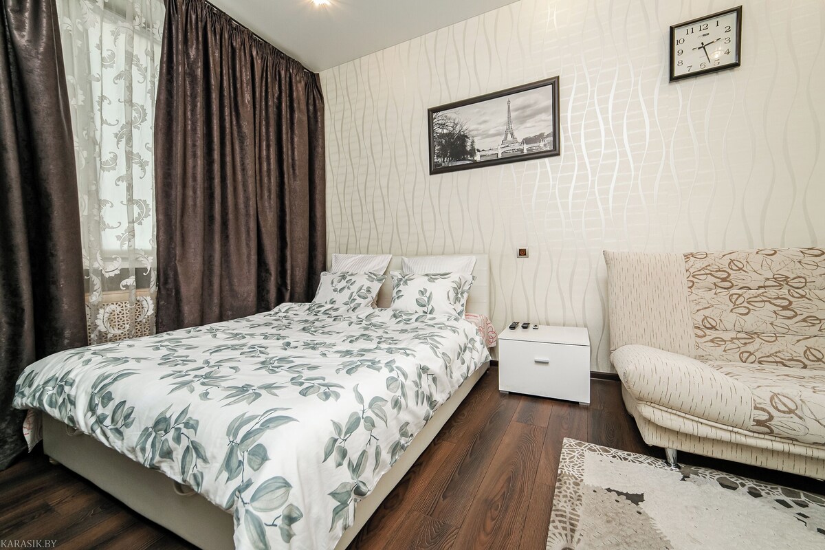 A bedroom with a bed, a nightstand, a chair, a clock, and a picture on the wall.