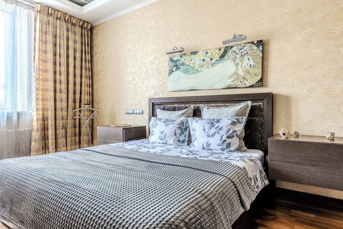A neatly made bed with a patterned bedspread, a headboard with a decorative design, and a painting above the bed.