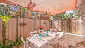An outdoor patio with a table set for dining, surrounded by a wooden fence, and a large shade sail overhead. - Yamba Daze Sunset - Walk to the pet-friendly beach from your pet-friendly stay (Yamba)