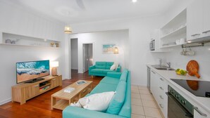 A modern living room with a teal sofa, a wooden coffee table, and a flat-screen TV. - Yamba Daze Sunset - Walk to the pet-friendly beach from your pet-friendly stay (Yamba)