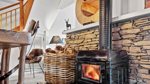 Ein gemütliches Wohnzimmer mit Kamin aus Stein, einem Korb aus Weidengeflecht mit Tannenzapfen und einem Holzstuhl.